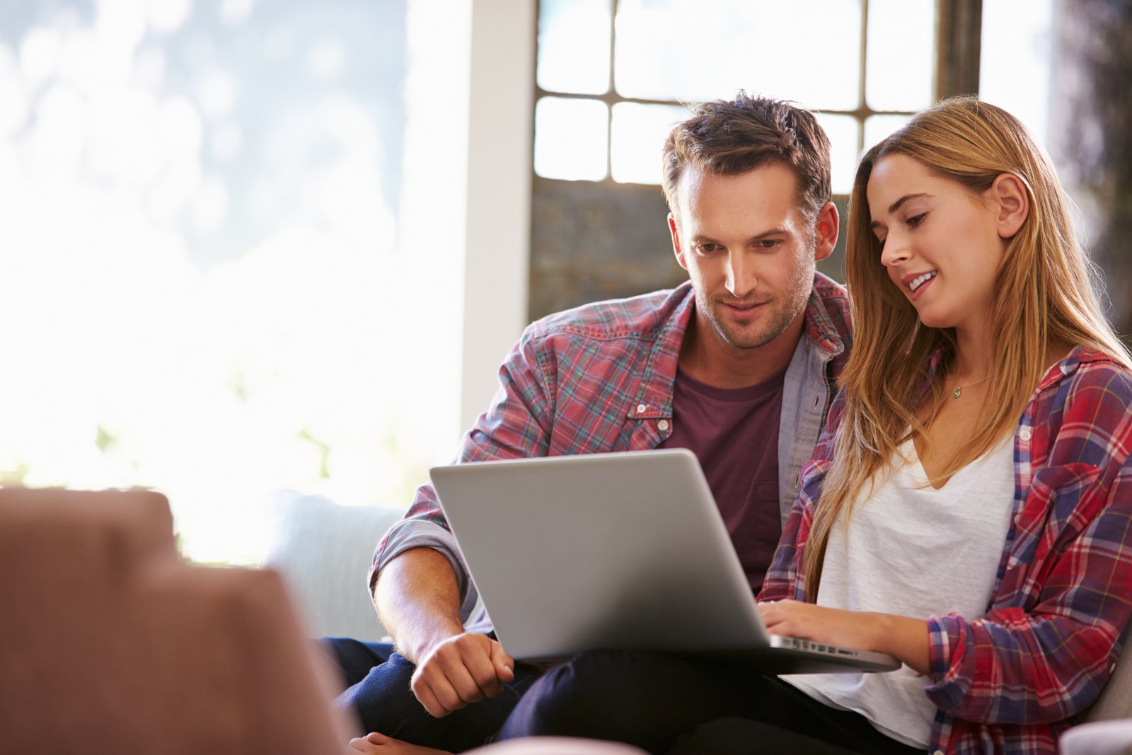Junges Paar sitzt zu Hause auf dem Sofa und schaut gemeinsam auf einen Laptop