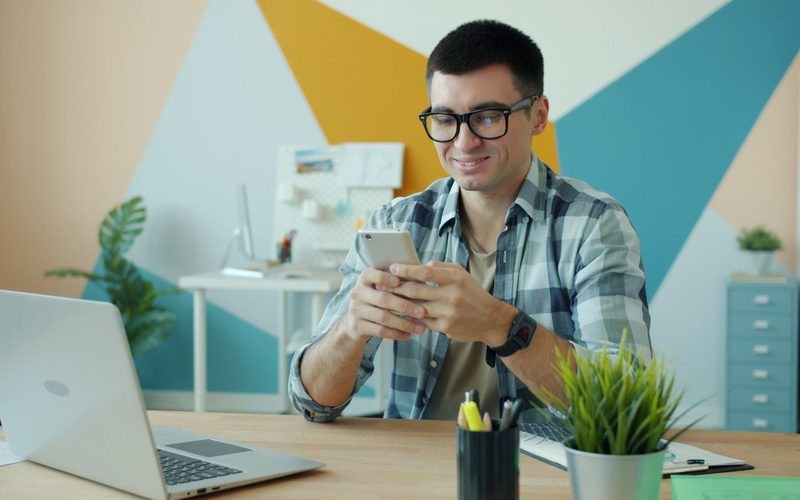 Mann sitzt lächelnd mit Smartphone am Schreibtisch